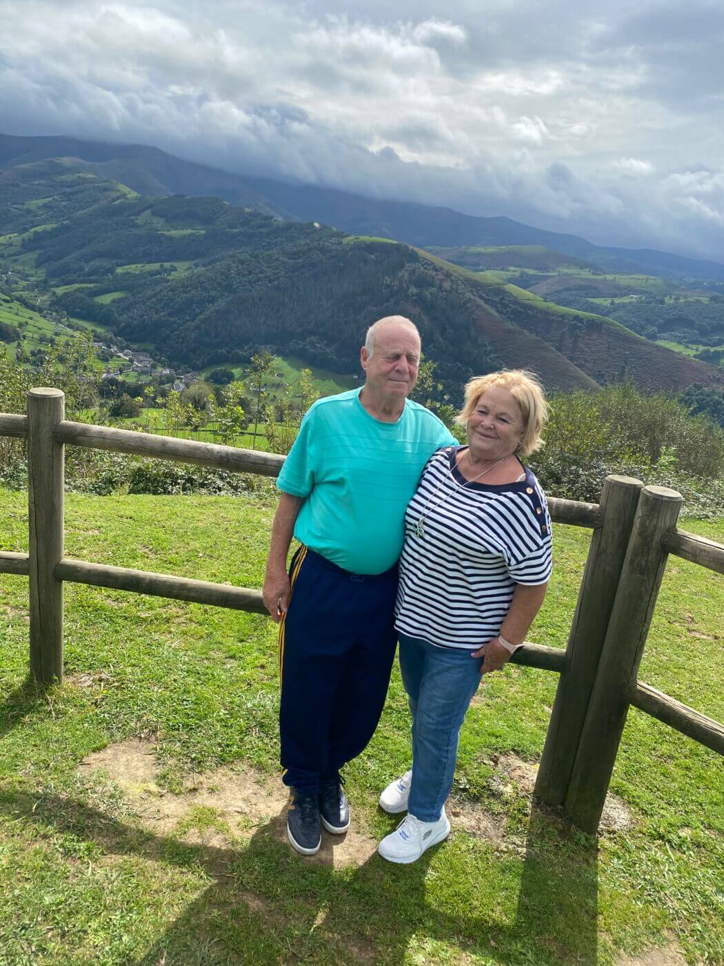 Pareja de edad abrazada al aire libre frente a un paisaje de montaña