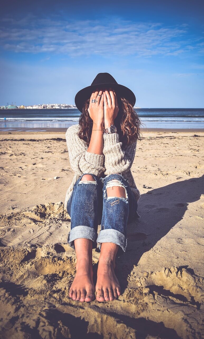 Mujer sentada en la playa cubriéndose el rostro con las manos, simbolizando la evitación emocional y la introspección