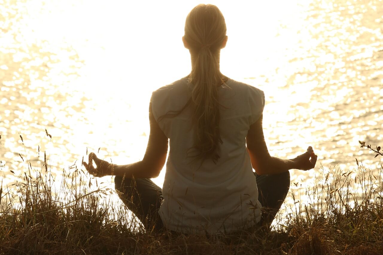 Mujer sentada frente a un lago al atardecer, en actitud reflexiva. Imagen sobre dolor crónico y conexión con el cuerpo.