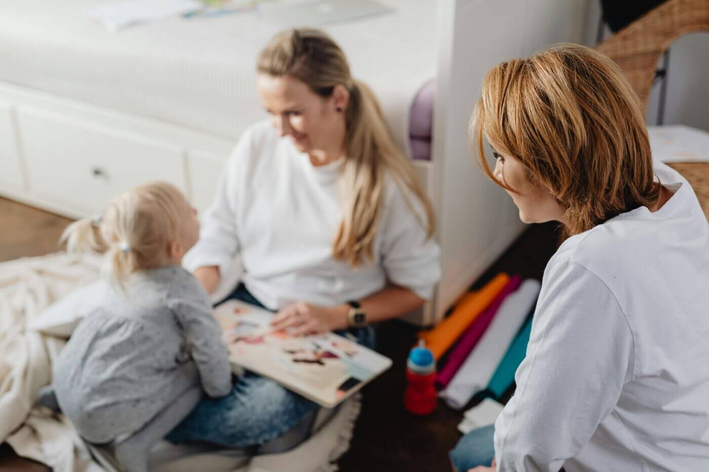 A heartwarming family scene of a mother, child, and friend enjoying reading and playing indoors.